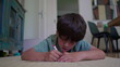 © Marco - Boy lies on floor concentrating while drawing with red marker, indoor environment with furniture and patterned artwork in background