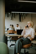 © BGStock72 - Woman talking on phone while sitting in office with coworkers in background