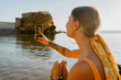 © mary_markevich - attractive young smiling blonde happy woman in yellow swimsuit sitting on beach on summer vacation using smartphone taking photo
