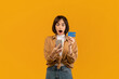 © Prostock-studio - Bonus and cashback concept. Surprised young lady showing debit credit card and using her smartphone, making online payment over yellow studio background