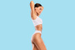 © Prostock-studio - Bodycare Concept. Profile Side View Portrait Of Slim Woman With Perfect Ideal Body Shape Posing With Raised Arms Isolated On Blue Studio Background, Wearing White Top And Panties, Free Copy Space
