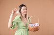 © New Africa - Easter celebration. Smiling woman in dress with wicker basket full of painted eggs on beige background