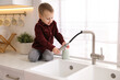 © New Africa - Child safety at home. Little boy pulling down faucet hose on counter in kitchen