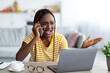 © Prostock-studio - Nervous young black woman independent contractor sitting in front of laptop, working from home, fighting on phone with clients or colleagues, gesturing and yelling, living room interior, copy space
