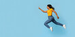 © Prostock-studio - Excited young black pretty lady jumping towards copy space, emotional african american woman running in the air and pointing at advertisement over blue studio background, panorama, web-banner