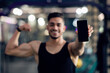 © Prostock-studio - Fitness App. Sporty Muscular Arab Man Holding Smartphone With Blank Black Screen And Showing Biceps At Camera, Athlete Guy Recommending Workout Application While Standing In Modern Gym, Mockup
