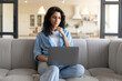 © Prostock-studio - Freelancing, online job or education concept. Serious young woman sitting on couch with laptop computer, working or studying from home. Attractive millennial lady having remote business meeting on pc