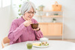 © buritora - A gray-haired senior woman eating in the dining room at home