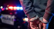© CK Studio - Person's hands in metal handcuffs, with a blurred police car and flashing red and blue lights in the dark night background, symbolizing arrest and justice.