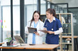 © Thitisak - Two female healthcare workers, one in blue scrubs and another in a white lab coat, are collaborating and reviewing patient charts on a clipboard and tablet. They are engaged in a professional discussi