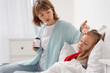 © Pixel-Shot - Mother with cough syrup checking her ill little daughter's temperature in bedroom