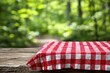 © PaniCreative - Red And White Gingham Tablecloth On Rustic Wooden Table In Forest With Bokeh Natural Background For Food Mockup Or Outdoor Picnic Setting