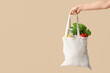 © Pixel-Shot - Female hand holding eco bag with different groceries on beige background