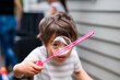 © NZstockphoto - A young child plays with a bubble wand, creating large bubbles outdoors in a backyard setting