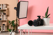© Pixel-Shot - Table with professional camera, houseplant and pink backdrop in modern photo studio, closeup