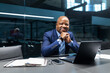 © Anastasiya - Confident black mature businessman sitting at conference table with hands folded, looking at camera in modern office, representing leadership, professionalism, and corporate success