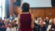 © Roberto - public speaking: a brunette professional manager woman with short hair wearing a dark red bordeaux blazer jacket speaking in public in the conference room