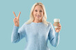 © Pixel-Shot - Mature woman with takeaway cup of coffee showing victory gesture on blue background