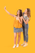 © Pixel-Shot - Female friends with mobile phone taking selfie on yellow background