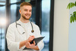 © Serhii - Smiling young doctor holding clipboard and writing notes