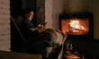 © olezzo - Happy young woman sitting by fireplace with smartphone in cozy winter interior