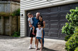 © NZstockphoto - Family stands smiling together outside a house, enjoying their time in a friendly atmosphere.