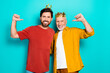 © deagreez - Two men wear crowns and smile together as friends and family in a bright turquoise studio