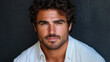 © sommersby - Striking close-up portrait of handsome man with curly dark hair and warm brown eyes, exuding confident and approachable demeanor against dark textured background, wearing light blue button-up shirt