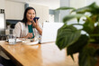 © Wavebreak Media - Mature woman holding smartphone to mouth, using white laptop in home kitchen with headset nearby