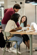 © Wavebreak Media - Diverse students leaning over round wooden table pointing to open book and laptop with coffee cup