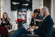 © qunica.com - A focused businessperson uses a laptop in a stylish office setup. Colleagues gather in the background, adding a collaborative and festive mood.
