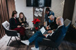 © qunica.com - A group of professionals gathers in a modern living room, using laptops and tablets. They collaborate around a small coffee table amid festive stockings and poinsettias.