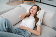 © InsideCreativeHouse - Woman relaxing on a couch, wearing headphones, eyes closed, enjoying music. Peaceful atmosphere, headphones providing a serene escape, relaxing moment. Music and entertainment image.