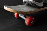 Angled close-up of a skateboard deck and red wheels on dark background. Minimal sports still life emphasizing motion, control, and urban lifestyle.