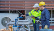 © reewungjunerr - Two professional engineers inspecting industrial air conditioning system outside. Construction workers checking hvac maintenance with clipboard and toolbox at manufacturing factory site plant.