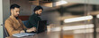 © Prostock-studio - Two men sit at a table in an office space. They focus on their laptops while a notebook and a cup are placed nearby. The atmosphere shows a typical work environment.