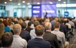 © FutureStock - Business presentation in office meeting room with blurred speaker and audience listeningRear view of large group of people attending business conference with blurred speaker on stage
