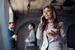 © Novak - Professional businesswoman in a suit talking on a smartphone with colleagues in the background.