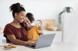 © Prostock-studio - Cute black mother and kid using laptop together, sitting at kitchen table with homemade pastry, hugging and looking at computer screen, spending time together, watching cartoon, copy space