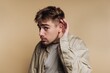 © bodnarphoto - Young man with hand to ear listening intently against beige background.