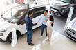 © Prostock-studio - Young middle-eastern couple visiting automobile showroom or exhibition, muslim man and woman embracing while having conversation with salesman, shaking hands, celebrating successful deal, top view