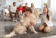 © Prostock-studio - Adorable kids playing and hugging pet dog while their big family relaxing on sofa in living room. Children having fun with golden retriever on floor at home, spending time with relatives indoors