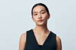 © SHOTPRIME STUDIO - Portrait of young woman with neutral expression wearing dark sleeveless top against plain light background, looking directly at camera in studio setting.