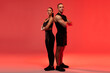 © Home-stock - Full body shot of strong fitness trainers standing back to back and looking at camera over red neon studio background, wearing black sportswear