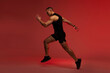 © Home-stock - Male runner running training over red neon studio background, side view, full length shot. Sportsman having workout wearing black sportswear