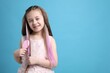© New Africa - Cute girl brushing her hair with pink clip-in extensions on light blue background. Space for text