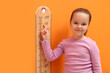 © New Africa - Little girl measuring her height with chart near orange wall