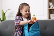 © New Africa - Girl packing her backpack for school on sofa at home