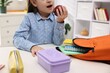 © New Africa - Girl with apple packing her backpack for school at desk indoors, closeup