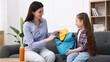 © New Africa - Mother and daughter packing backpack for school on sofa at home